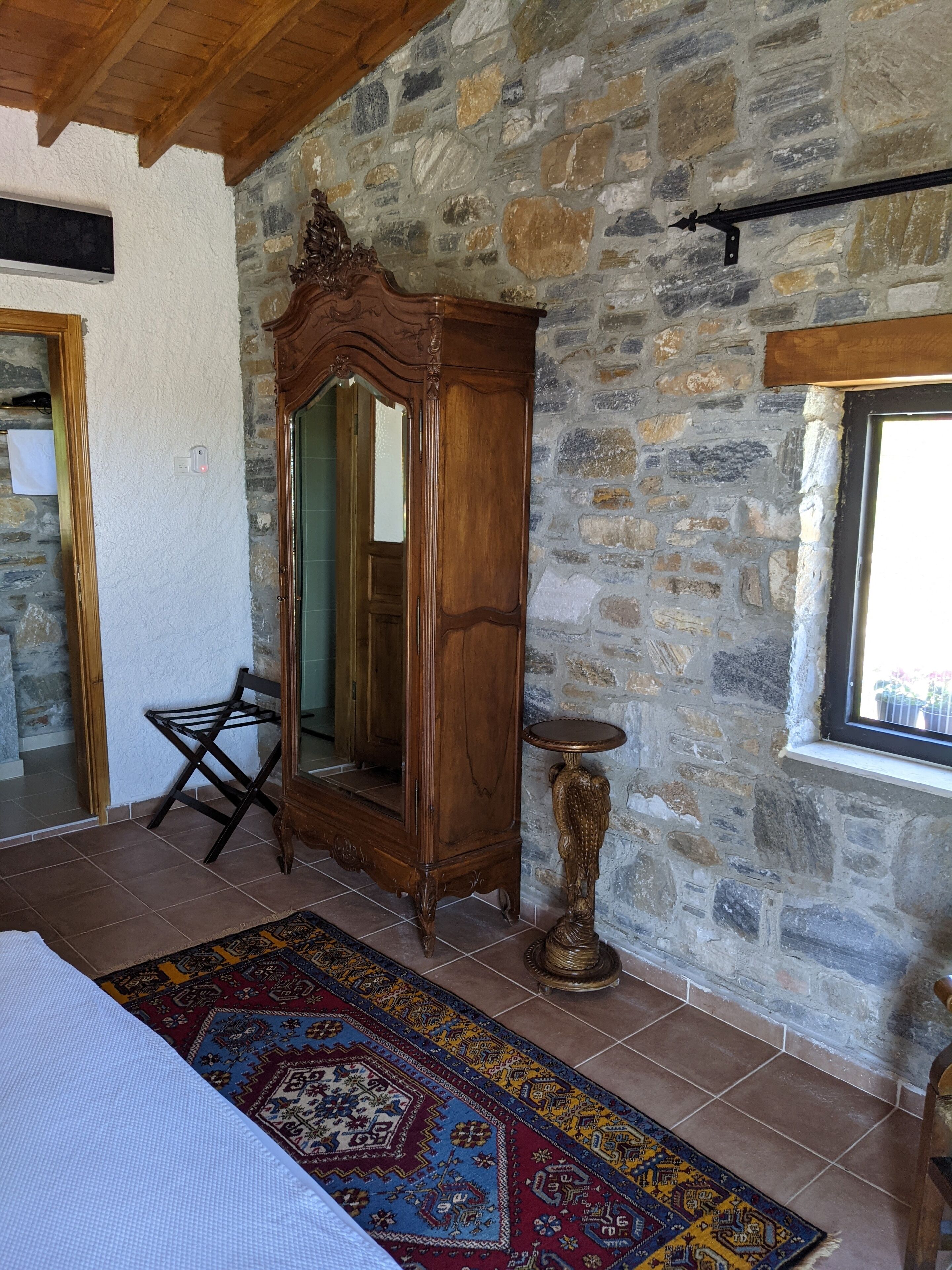 Una habitación con pared de piedra, un armario de madera, un espejo, una mesita pequeña y una alfombra estampada.