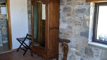 Una habitación con pared de piedra, un armario de madera, un espejo, una mesita pequeña y una alfombra estampada.