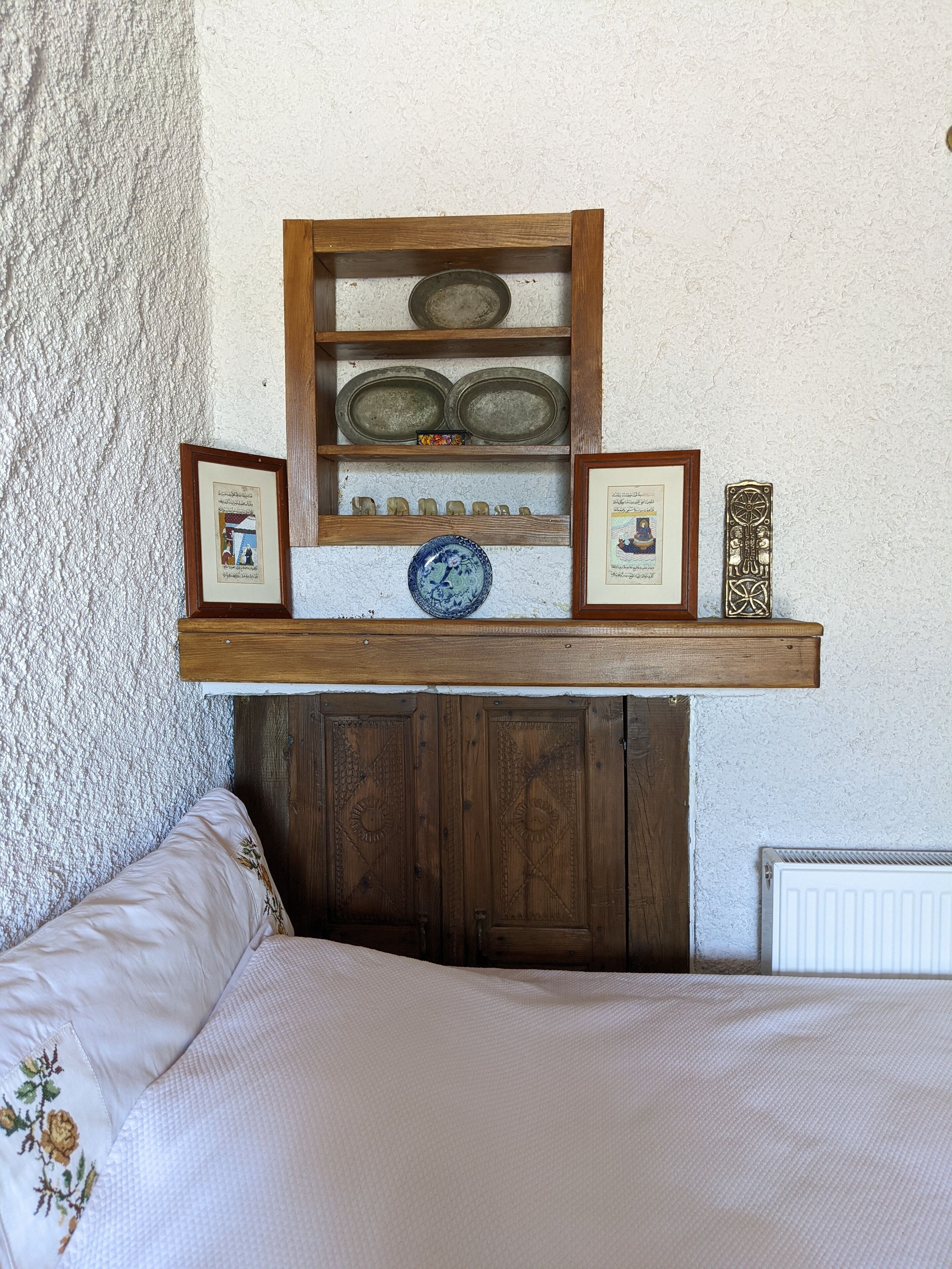 Ein Schlafzimmer mit einem hölzernen Regal über dem Bett, auf dem gerahmte Bilder und dekorative Teller stehen.