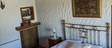 A bedroom with a bed, a wooden headboard, a ceiling fan, a wall-mounted air conditioner, a framed artwork, a bedside table, and a small cabinet.