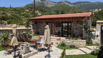 A stone building with a red-tiled roof, outdoor seating, and a view of mountains.