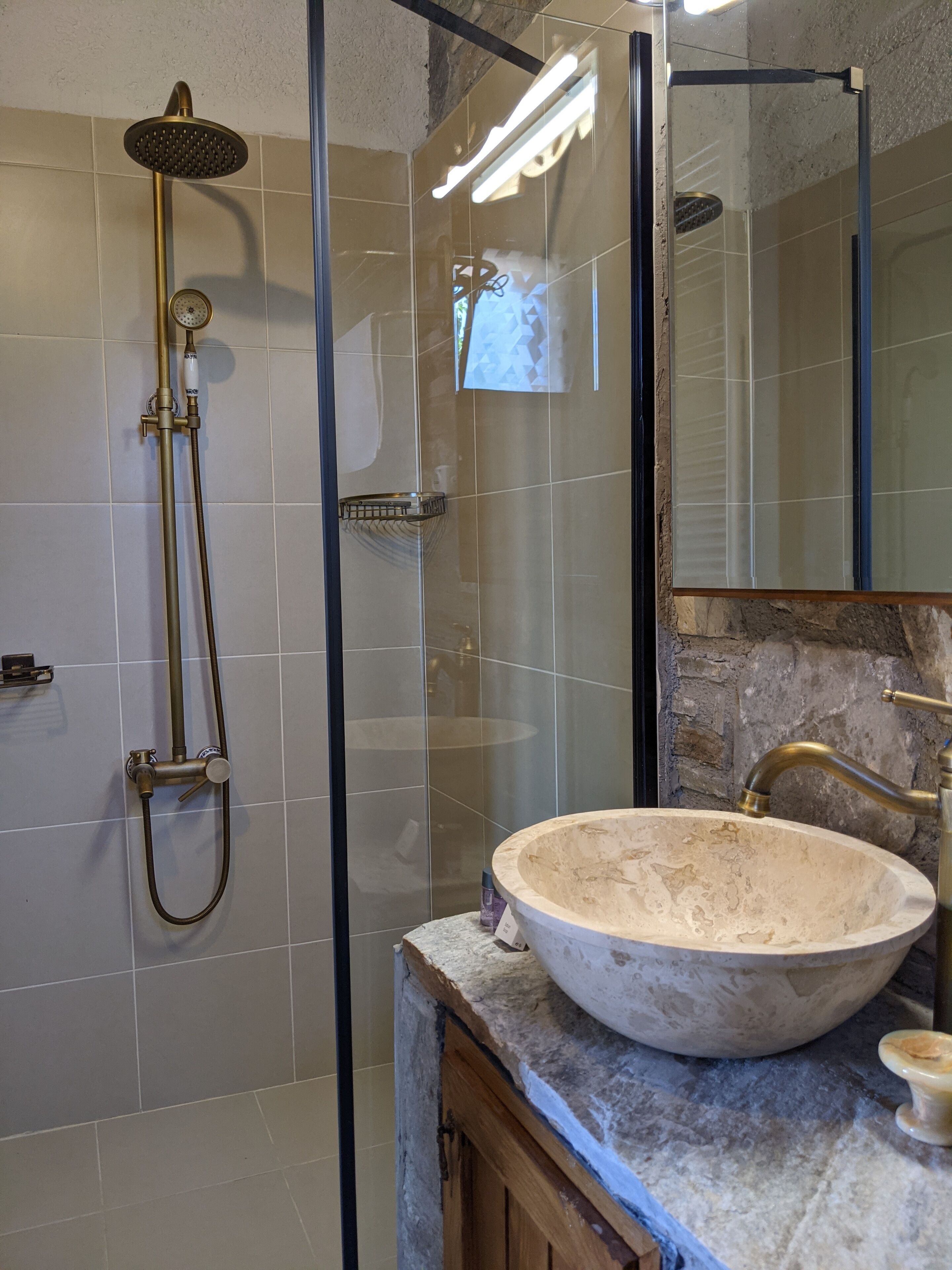 Un baño moderno con ducha envuelta en vidrio, lavamanos de mármol y un espejo grande.