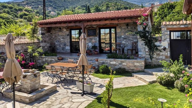 A stone building with a tiled roof, outdoor seating, and a view of mountains. - Bahab Guest House (Soke)