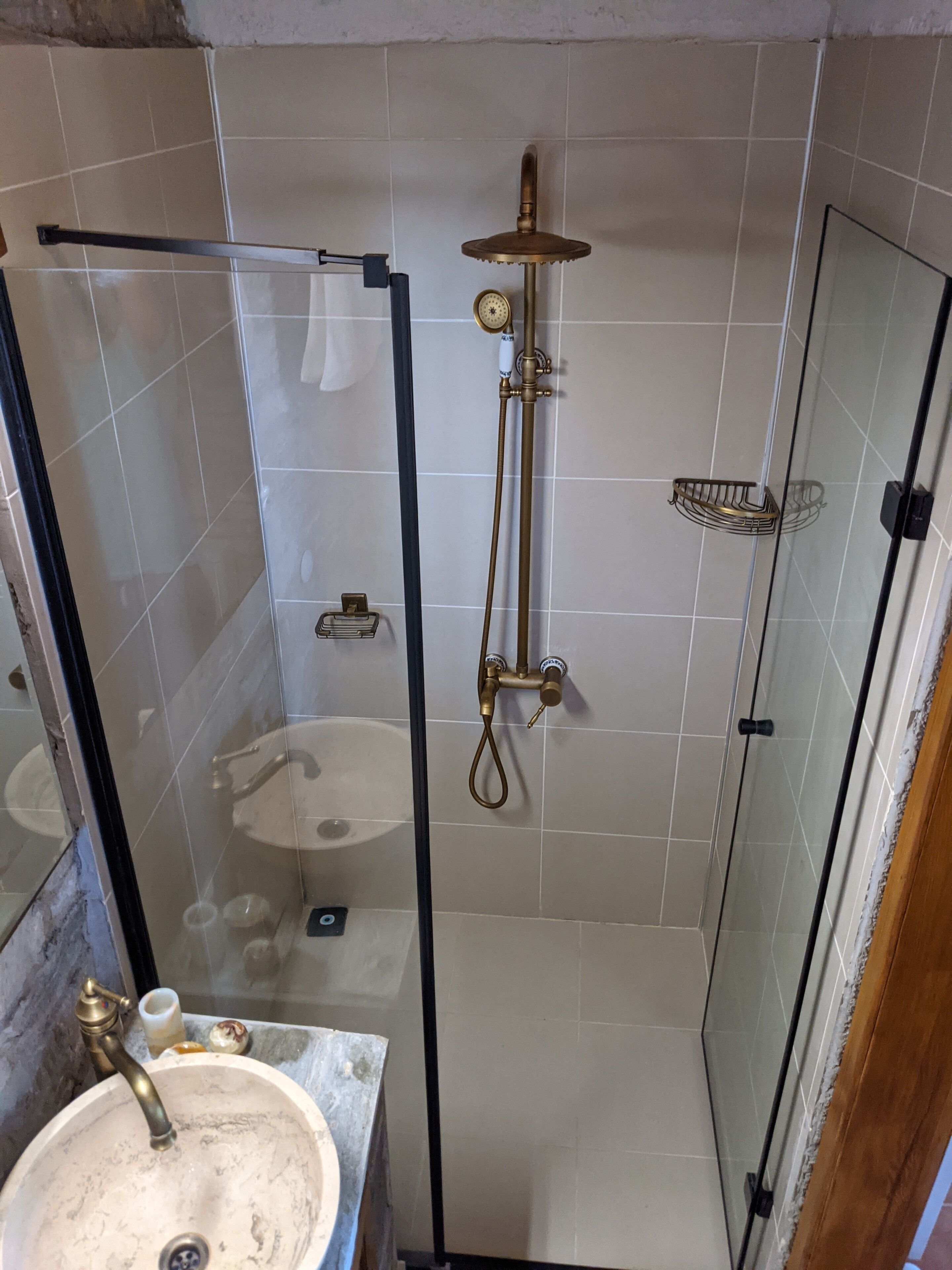 Ducha con cerramiento de vidrio, cabezal de ducha de mano y puerta de vidrio.