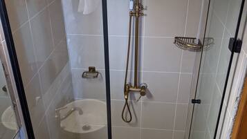 Ducha con cerramiento de vidrio, cabezal de ducha de mano y puerta de vidrio.
