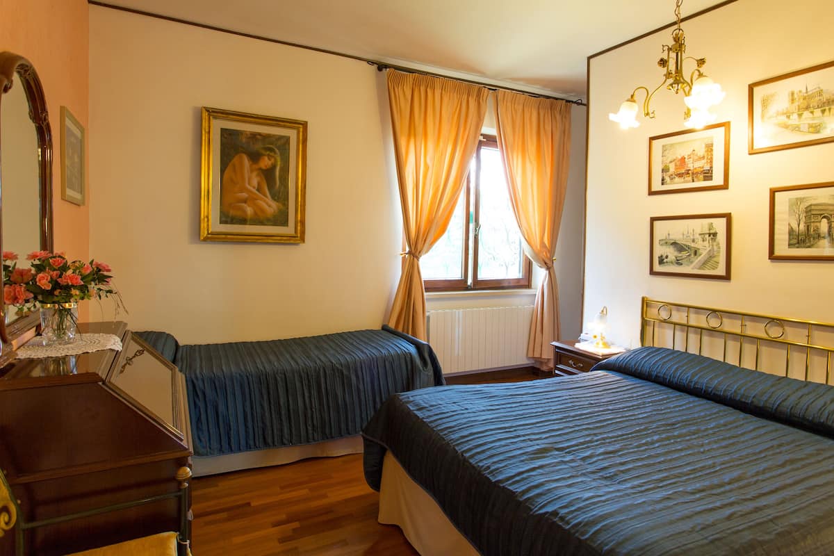 Quarto com duas camas de solteiro, cómoda de madeira, um vaso de flores e várias molduras nas paredes.
