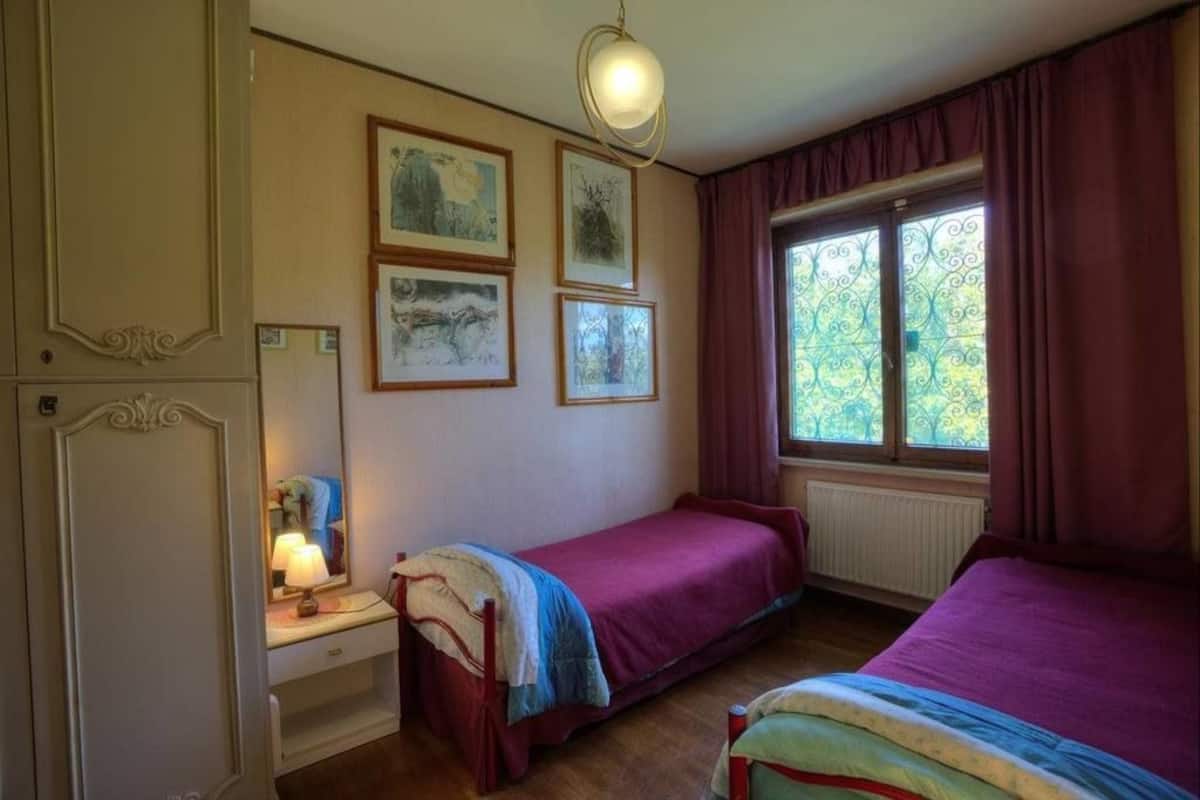 Quarto com duas camas, uma mesa de cabeceira com abajur, cômoda e quadros na parede.