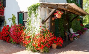 A rustic building with a wooden porch, potted plants, and a variety of flowers.