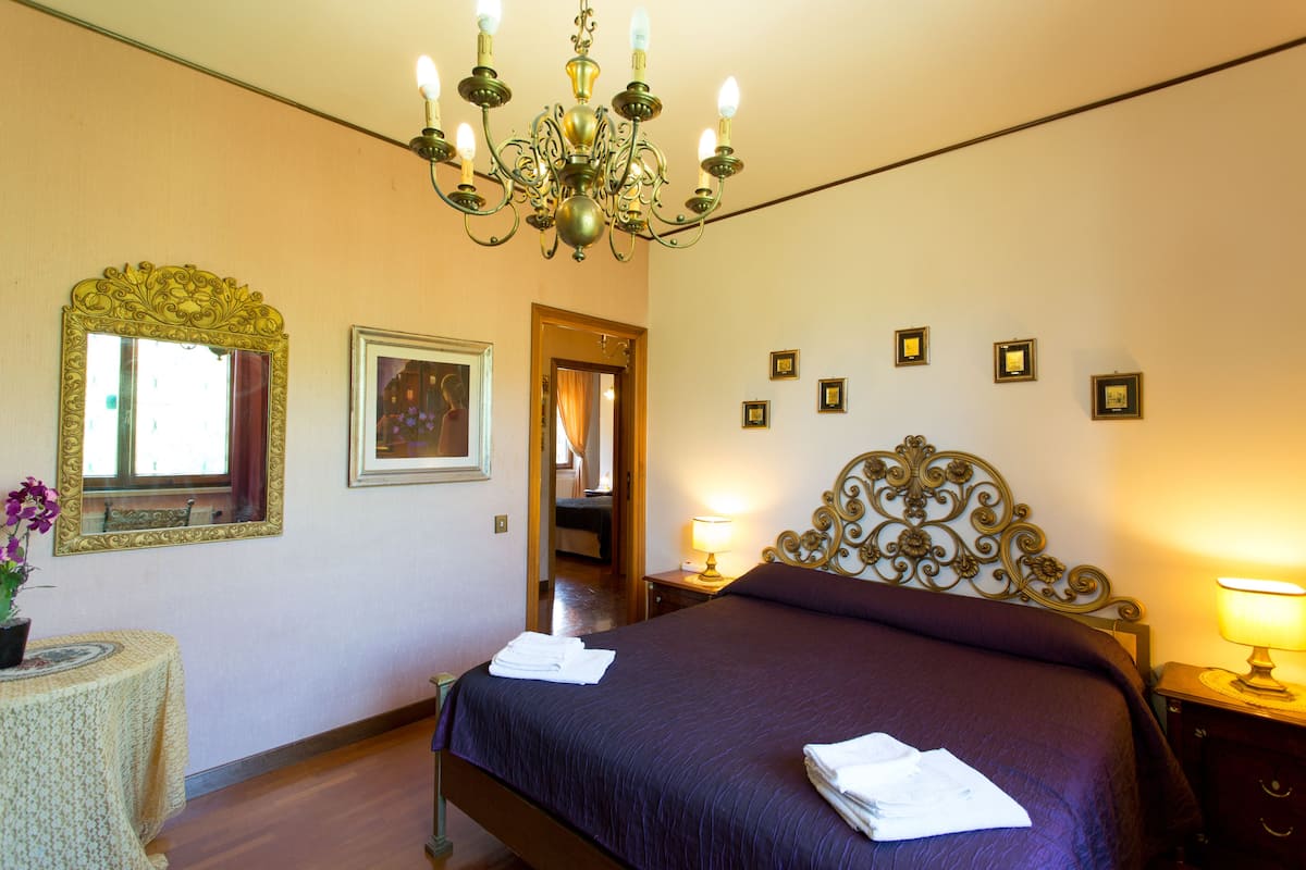 Quarto com cama, lustre, espelho e quadros nas paredes.