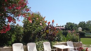 An outdoor seating area with white plastic chairs and a table, surrounded by lush greenery and flowering plants. - B&B Villa Sans Souci (Civitavecchia)