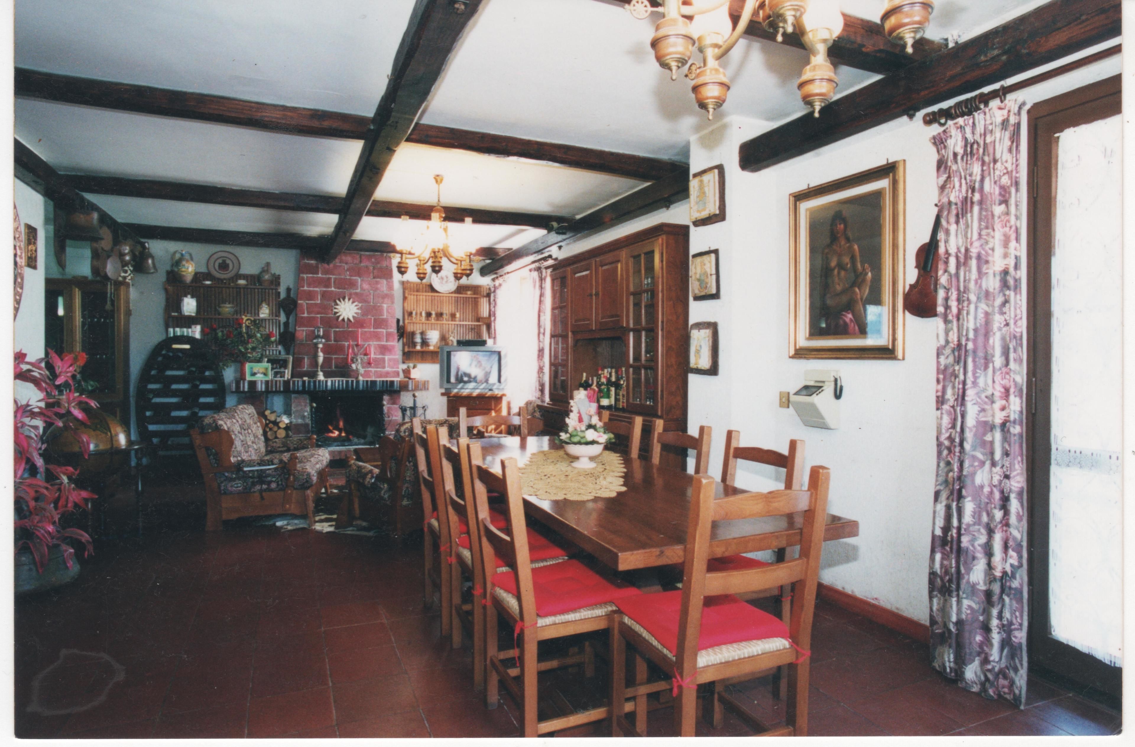 Un comedor con mesas y sillas de madera, una araña y una chimenea de ladrillo.