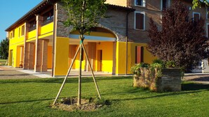 Una casa de dos pisos con fachada amarilla, una chimenea de ladrillo y un árbol en el patio delantero.