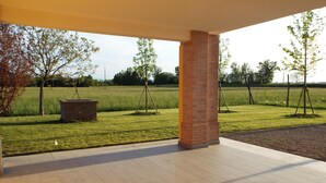 Un patio al aire libre con un columnilla de ladrillo, una jardinera de ladrillo y vista a un campo cubierto de césped y árboles.