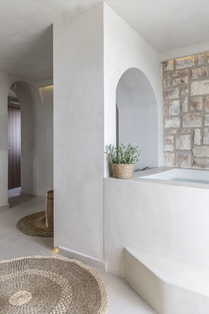 A modern interior with a stone wall, a white bathtub, and woven rugs.
