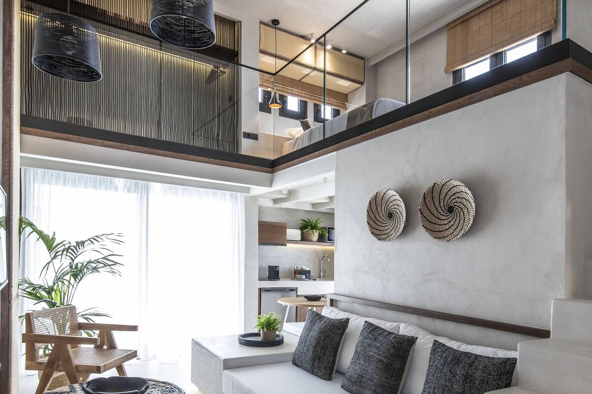 A modern living room with a white sofa, a round woven ottoman, and a staircase leading to an upper level.