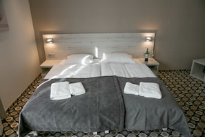 A neatly made double bed with a grey blanket, two white towels, and a bottle of wine on a bedside table. - Marina Mielno z widokiem na Jezioro (Mielno)