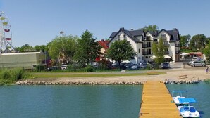 A waterfront property with a wooden dock, a Ferris wheel in the background, and a row of multi-story buildings with balconies.