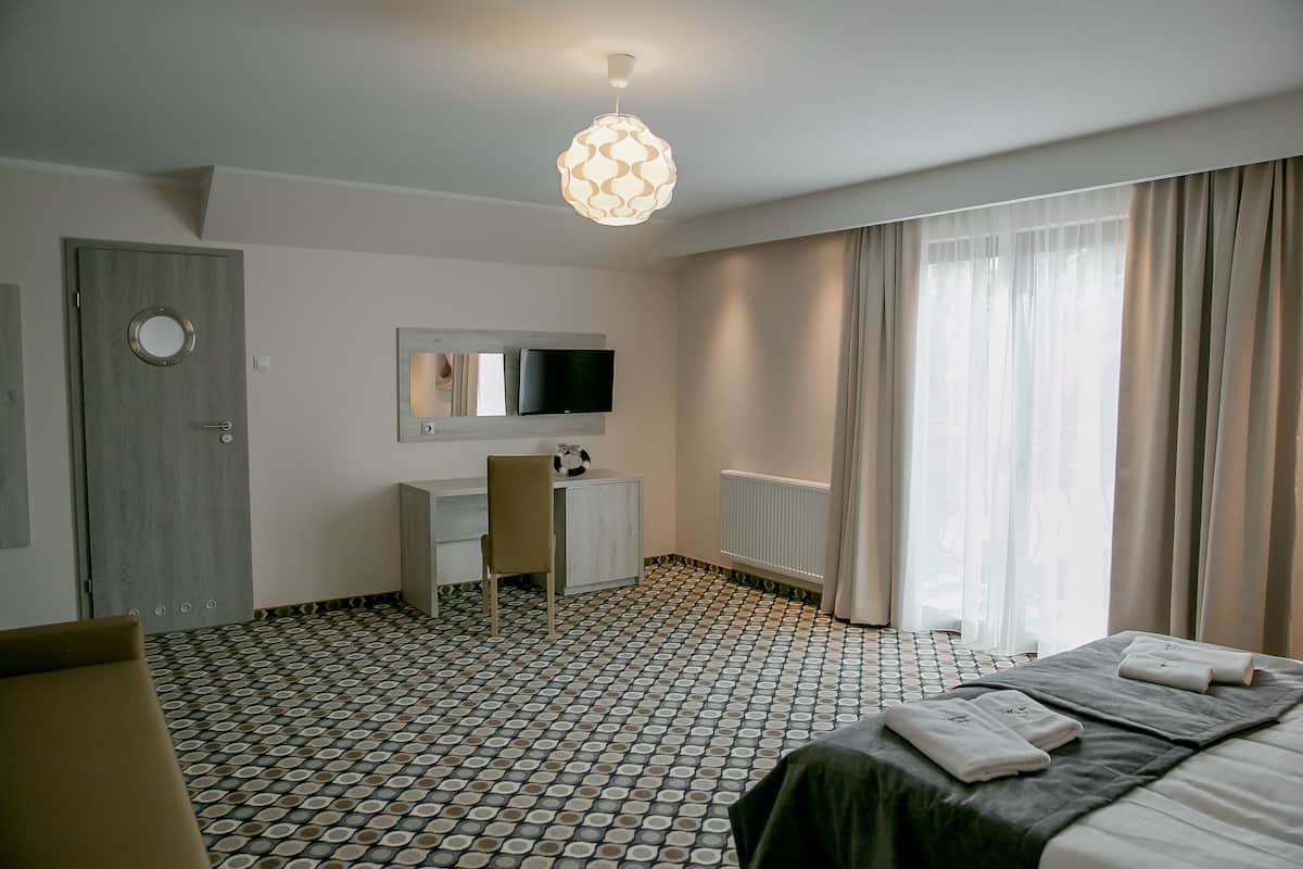 A hotel room with a bed, a desk with a chair, a TV, and a window with curtains.