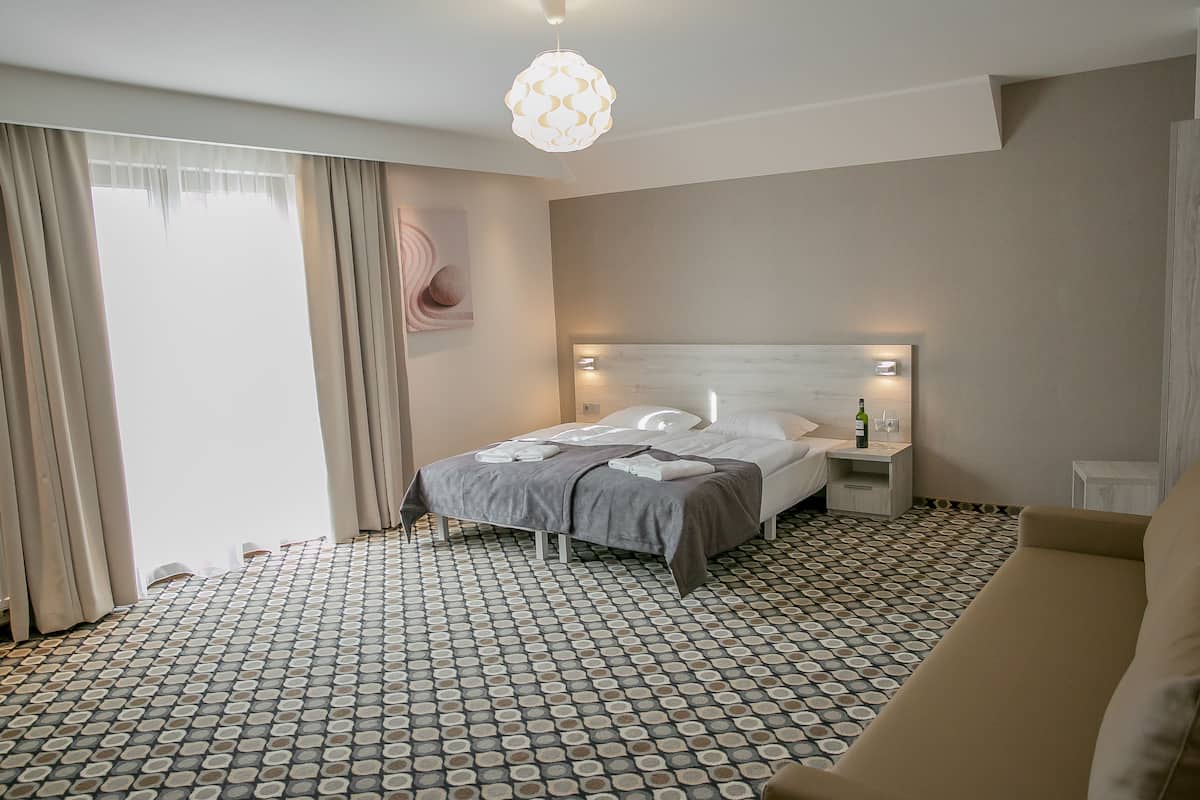 A hotel room with a bed, bedside tables, a sofa, patterned floor, and a hanging light fixture.