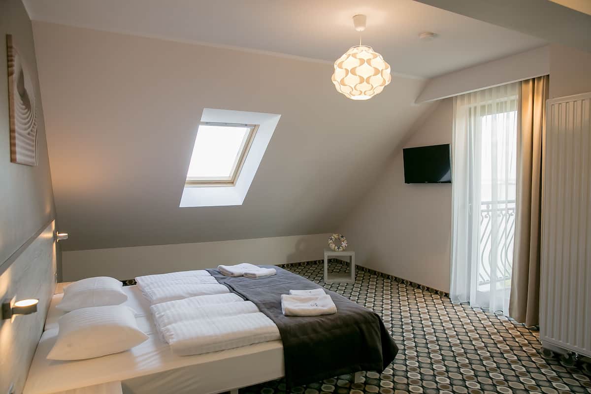 A hotel room with a bed, a small bedside table, a TV, a window, and a patterned floor.