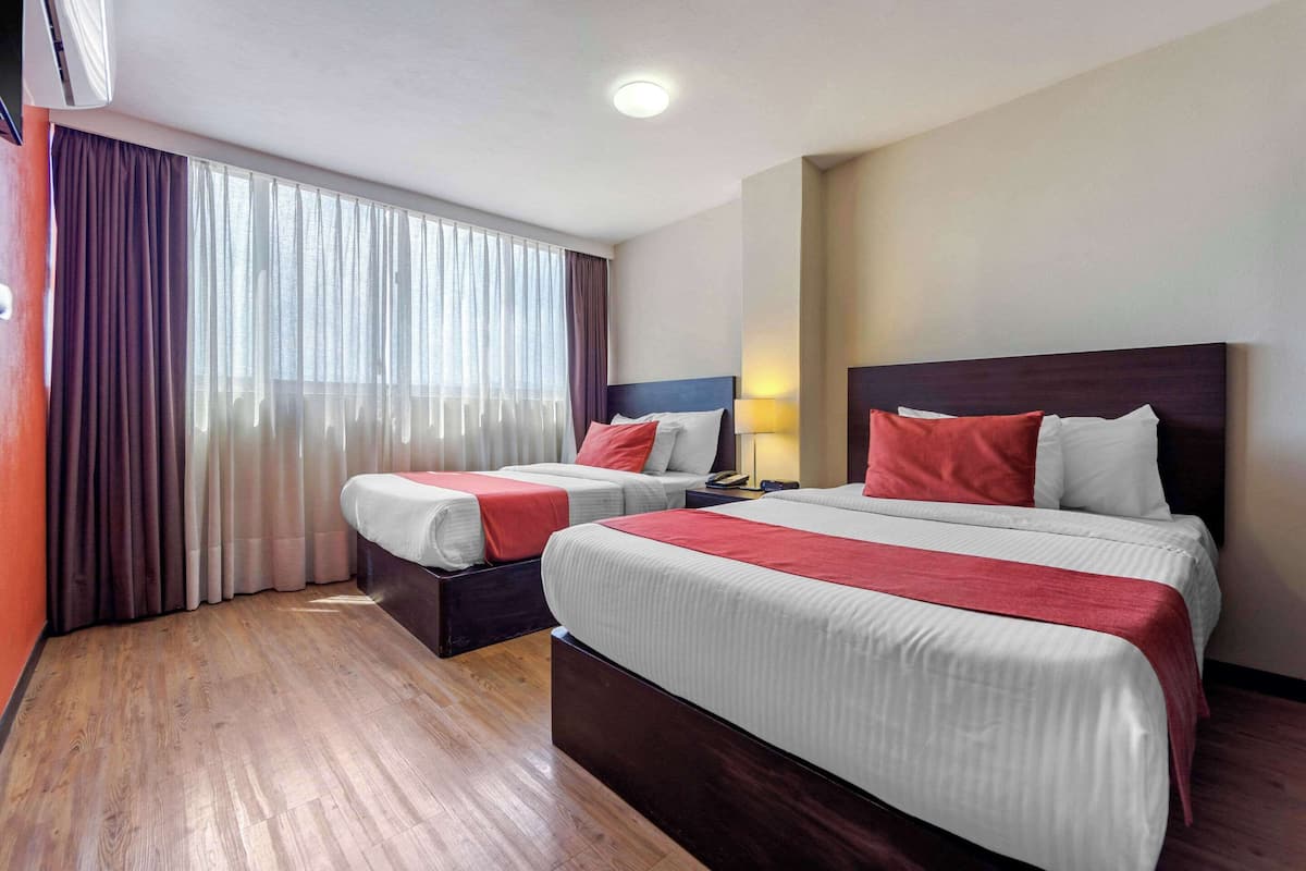 Hotellihuone, jossa on kaksi sänkyä, puulattia, suuri ikkuna verhoilla ja kattovalaisin.
