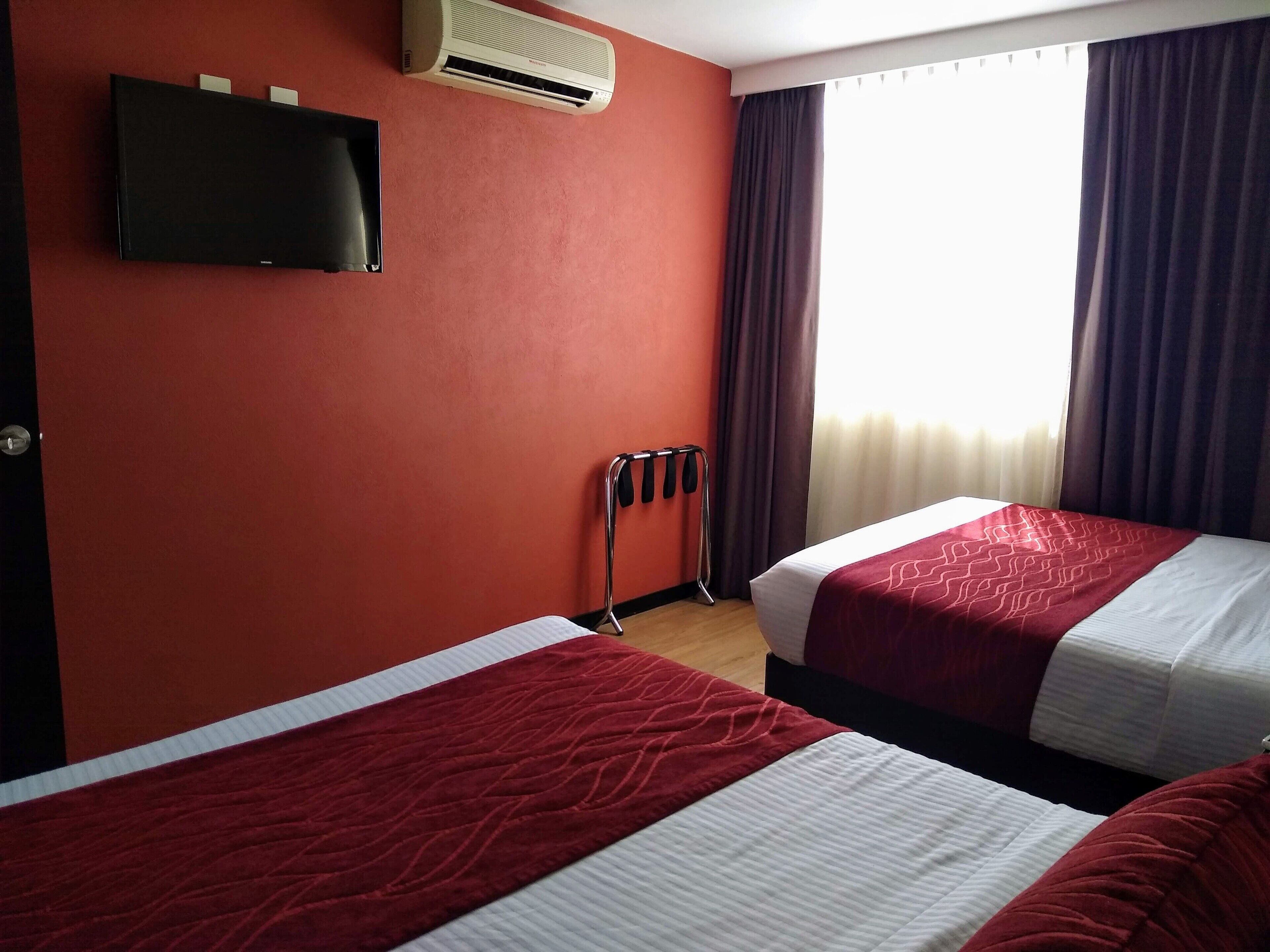 A hotel room with two beds, a TV mounted on the wall, an air conditioner, and a window with curtains.