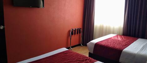 A hotel room with two beds, a TV mounted on the wall, an air conditioner, and a window with curtains.