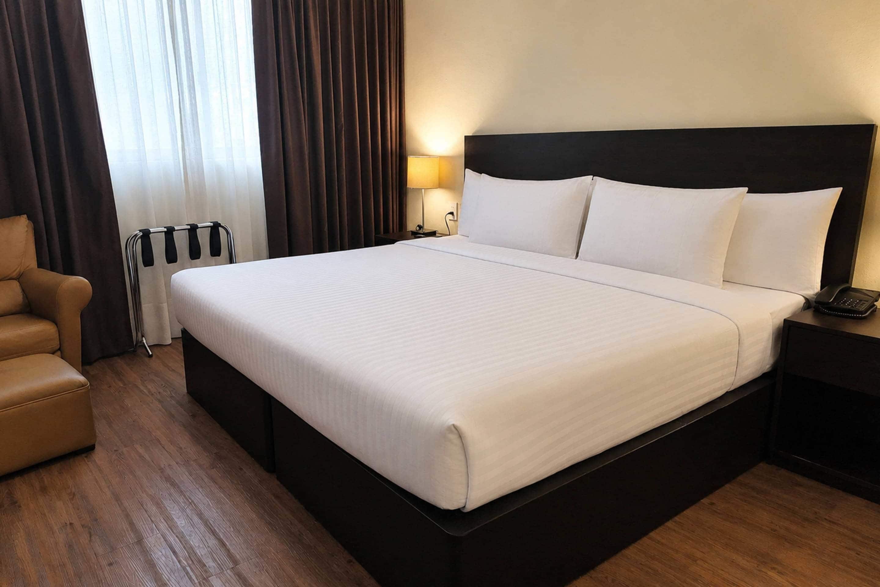 A hotel room with a large bed, a bedside table with a lamp, and a chair.