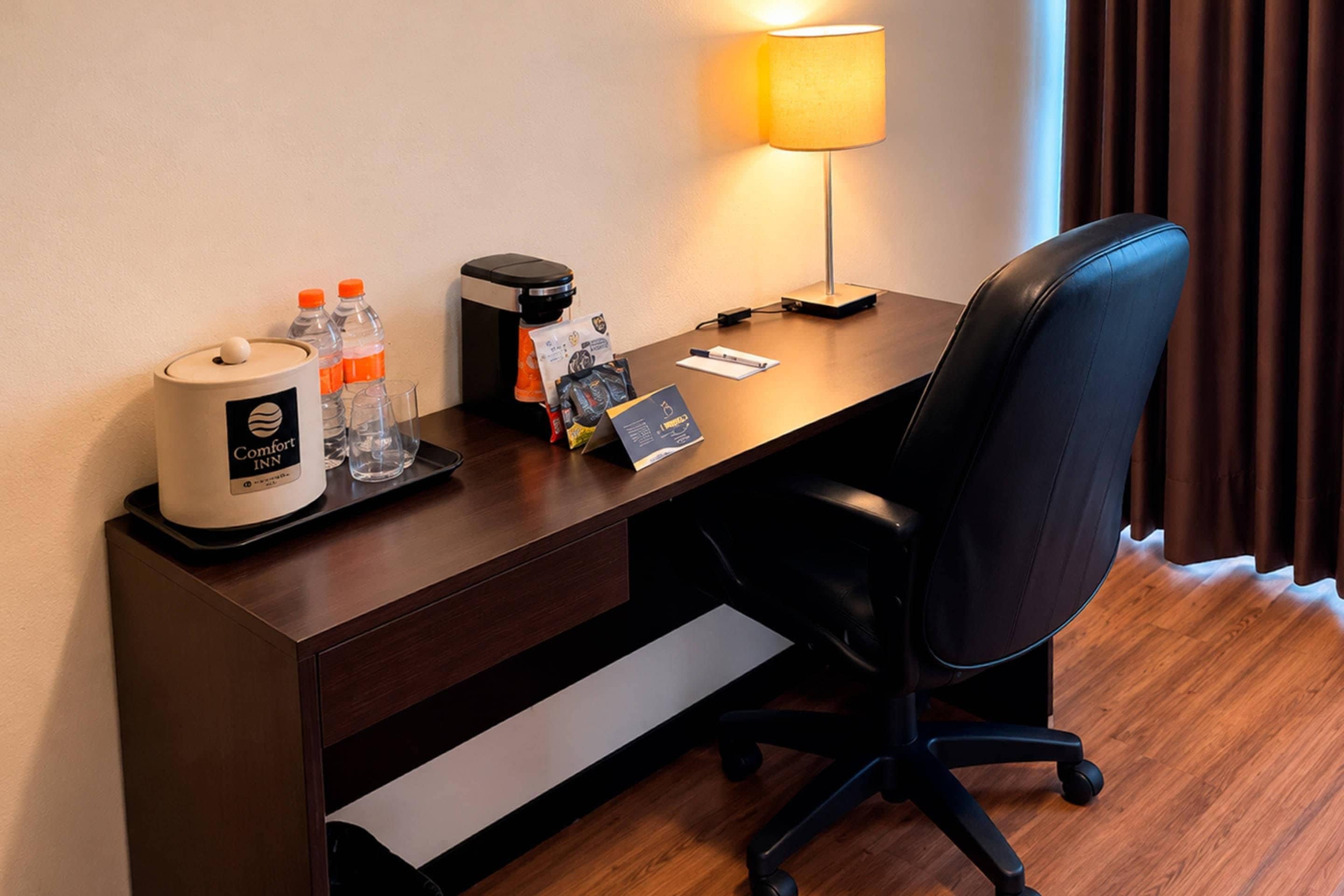 A hotel room desk with a coffee maker, water bottles, a tissue box, a lamp, and a chair.