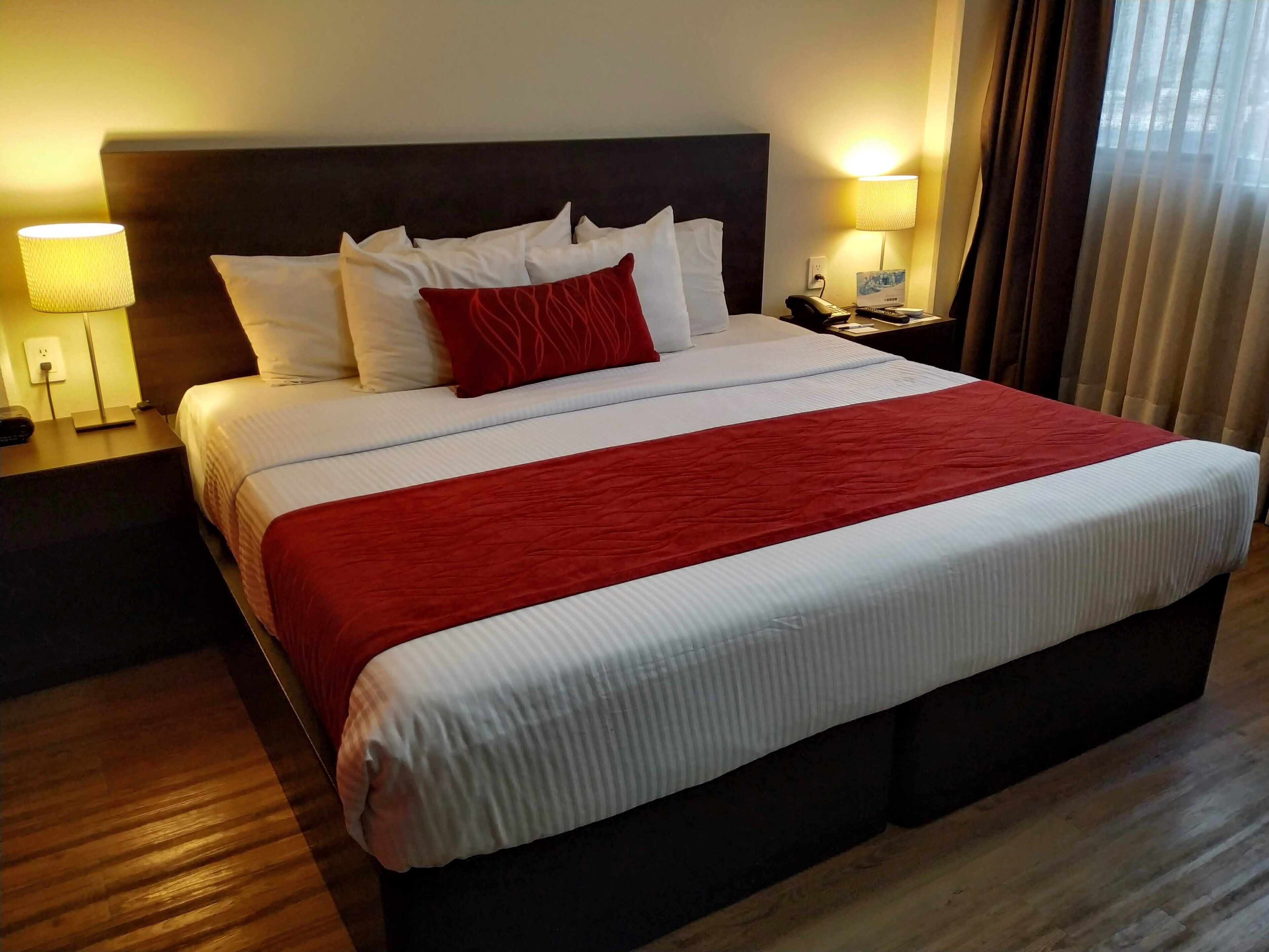 Una habitación de hotel con una cama grande, dos mesitas de noche y una lámpara.