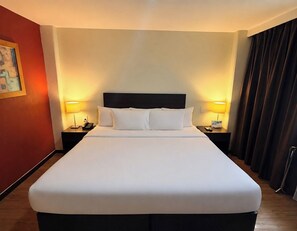 Une chambre d’hôtel avec un grand lit, deux tables de chevet avec des lampes, un tableau au mur et un rideau à la fenêtre.