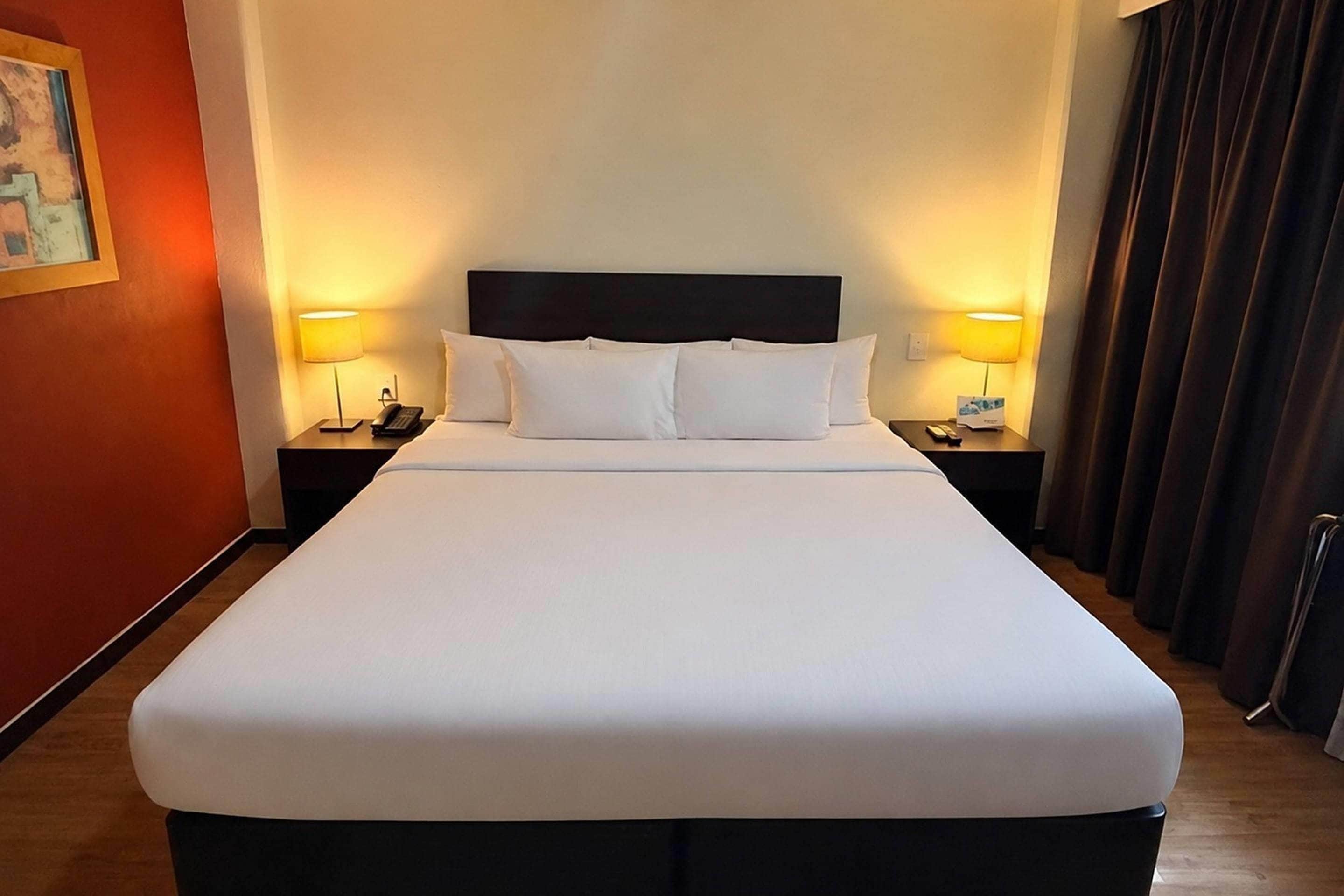 A large bed with white linens, two bedside tables with lamps, and a dark headboard.