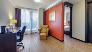 A hotel room with a wooden floor, a desk with a chair, a sofa, a bed, and a red accent wall. - Comfort Inn San Luis Potosi (San Luis Potosi)