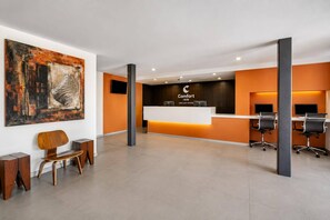 Un espace d’accueil d’hôtel au design moderne, comprenant un comptoir d’accueil, un coin salon et des œuvres d’art accrochées au mur.