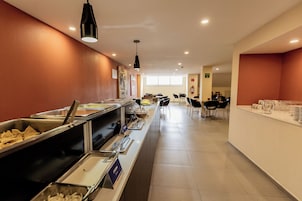 Un área de buffet con diversas opciones de comida, un espacio de estar con sillas y un mostrador con dispensador de agua.
