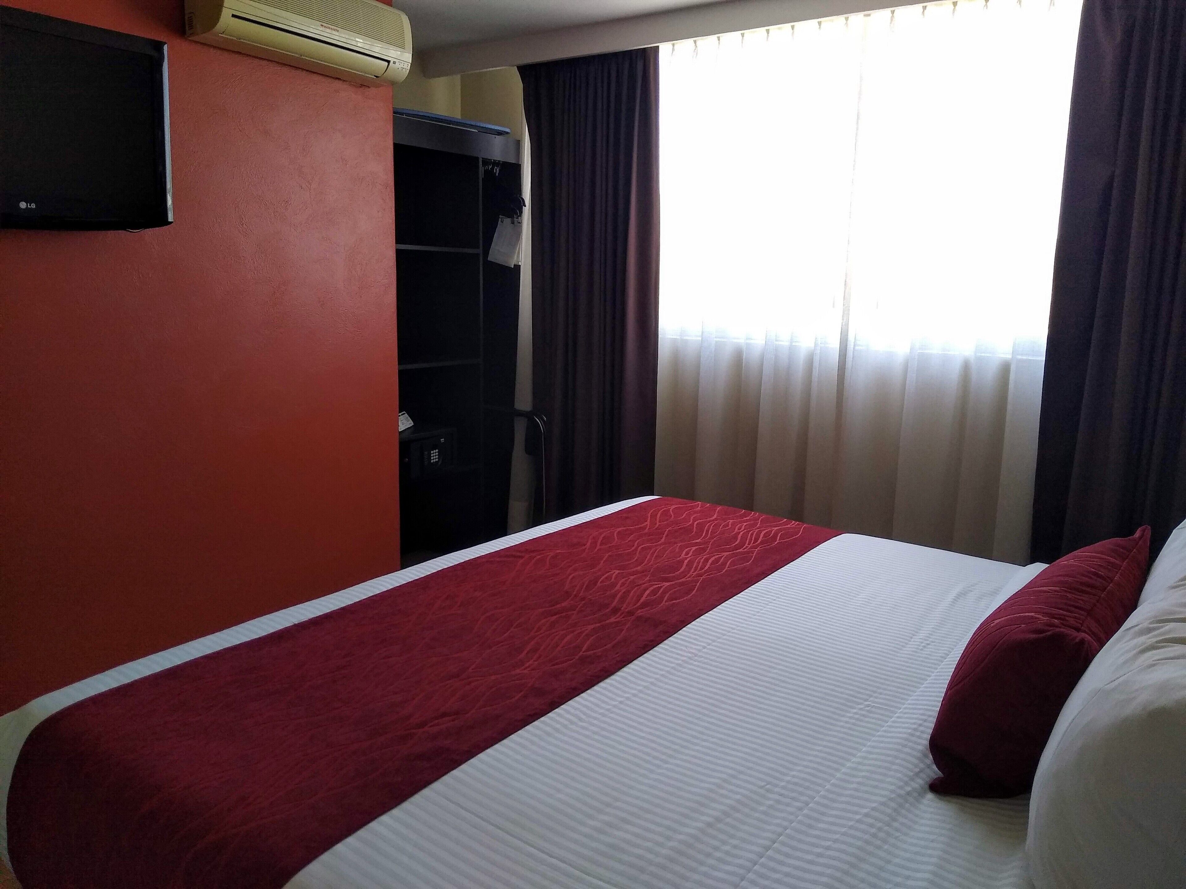 A hotel room with a bed, a wardrobe, and a window with curtains.