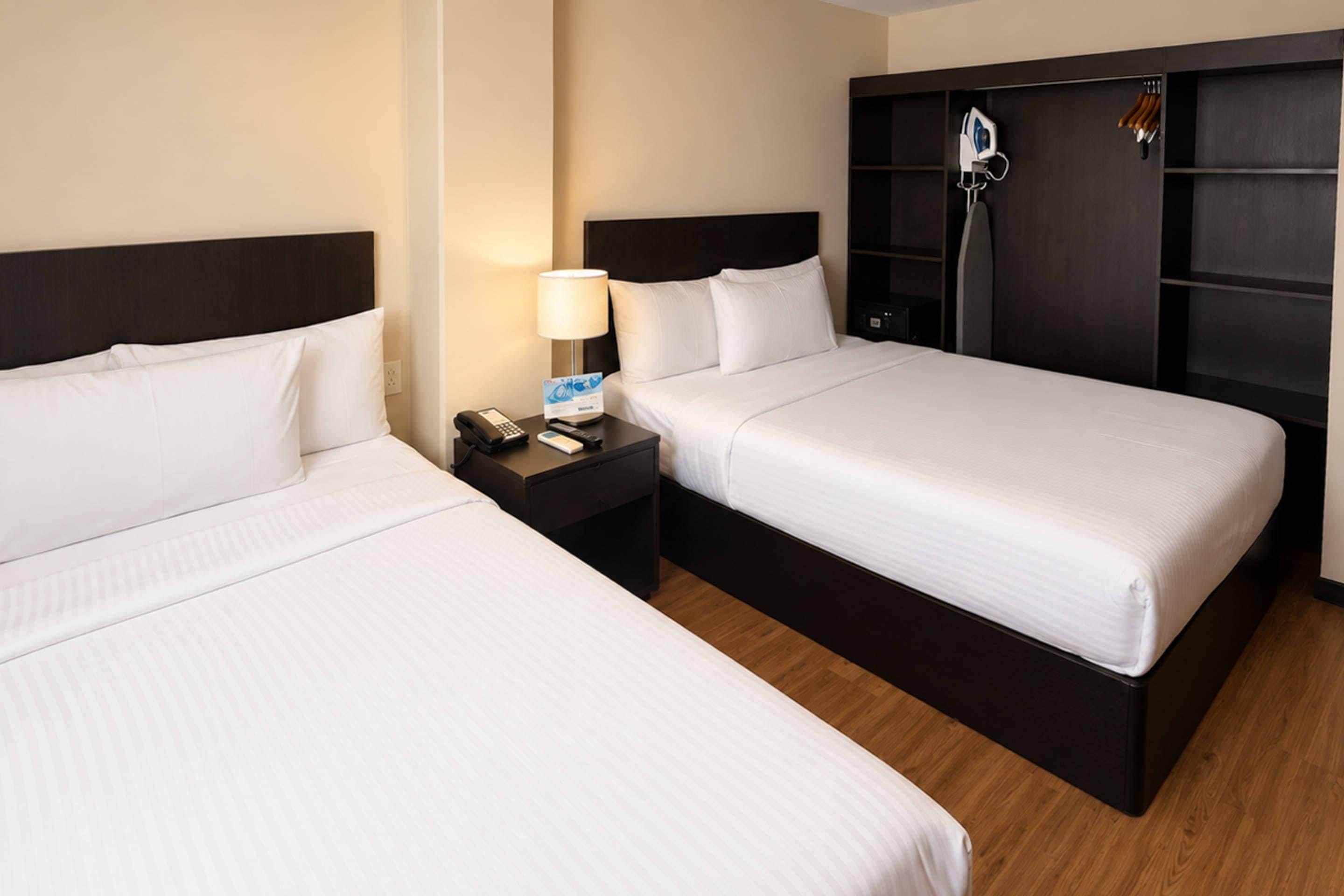 Habitación de hotel con dos camas, una mesita de noche con un teléfono y una tarjeta, y un armario de madera oscura con ducha.