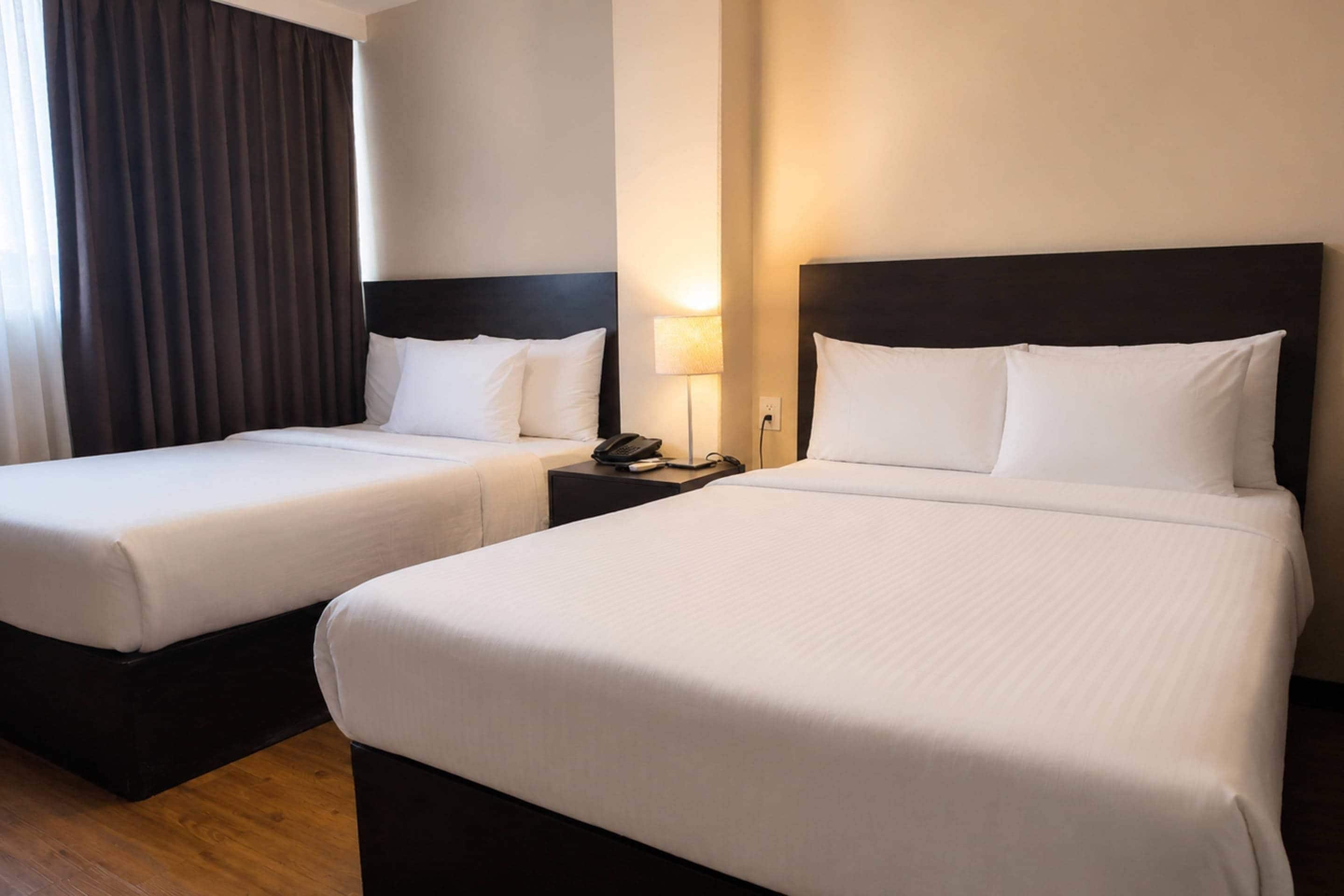 A hotel room with two beds, a nightstand with a lamp, and a window with curtains.