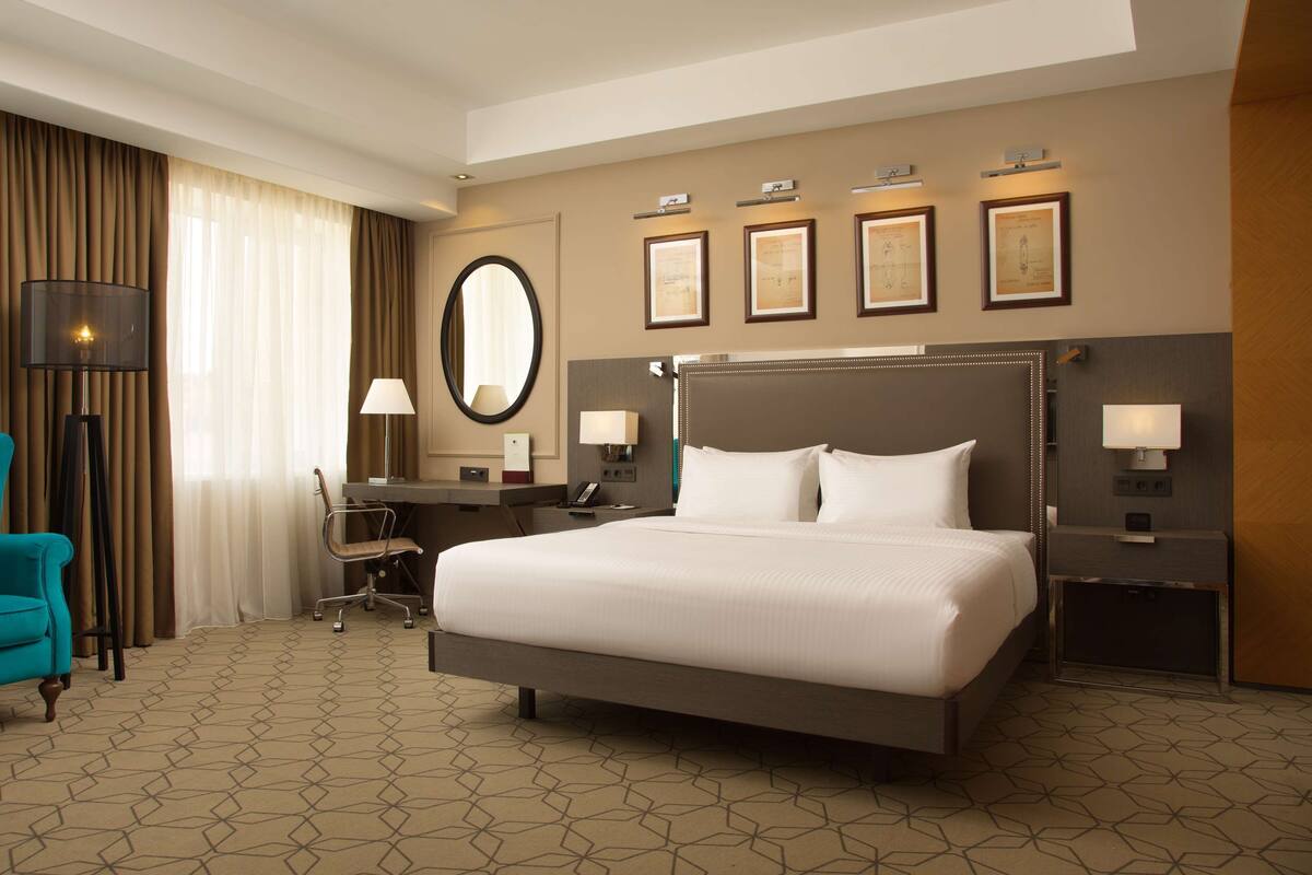 Habitación de hotel con una cama grande, un escritorio con silla, una lámpara de pie y un espejo amplio.