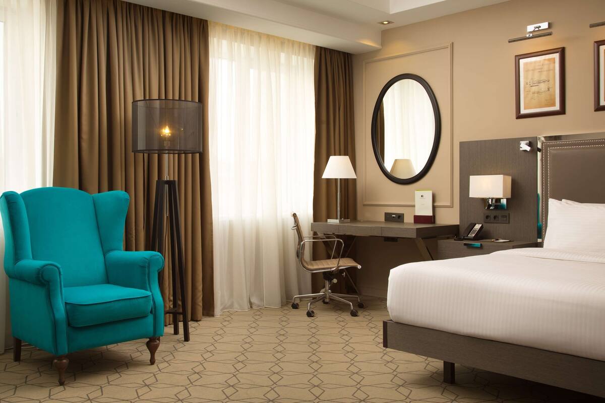 Habitación de hotel con cama, escritorio, silla, lámpara de pie y un espejo grande.
