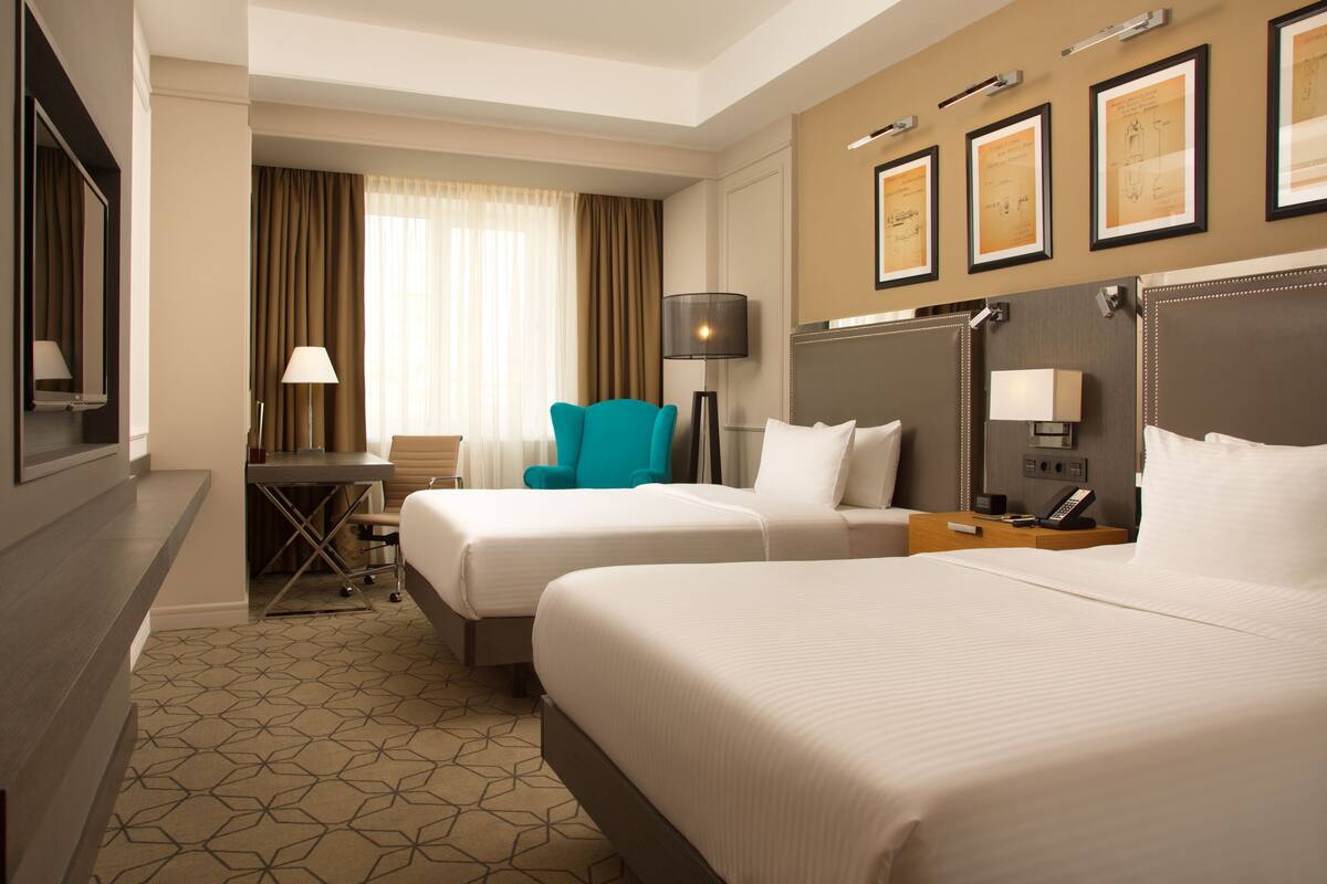 Una habitación de hotel con dos camas, un escritorio, una silla, una lámpara y diplomas enmarcados en la pared.