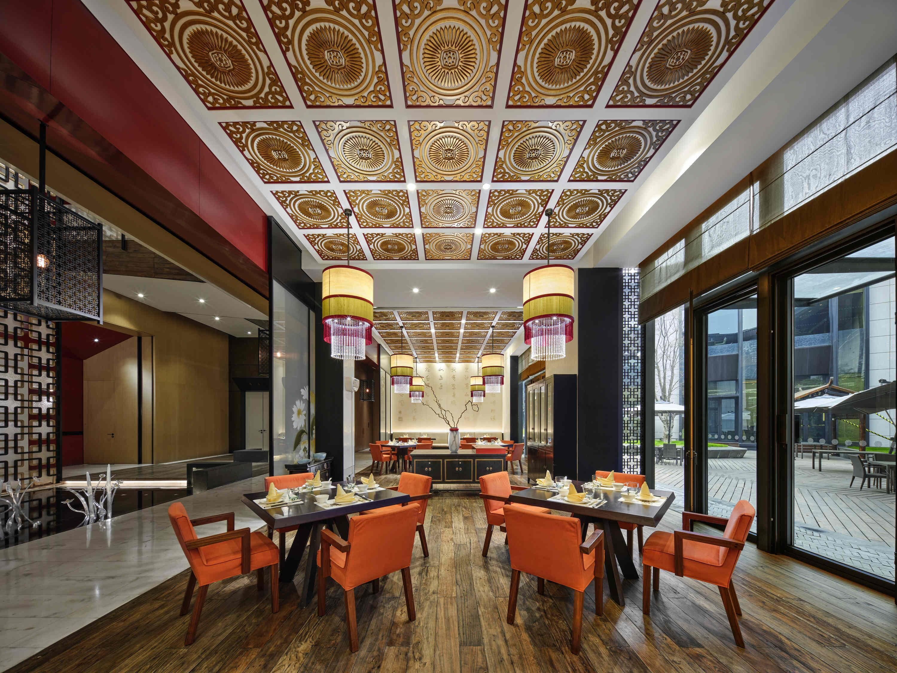 Restaurante com design tradicional no teto, piso de madeira e cadeiras laranja.