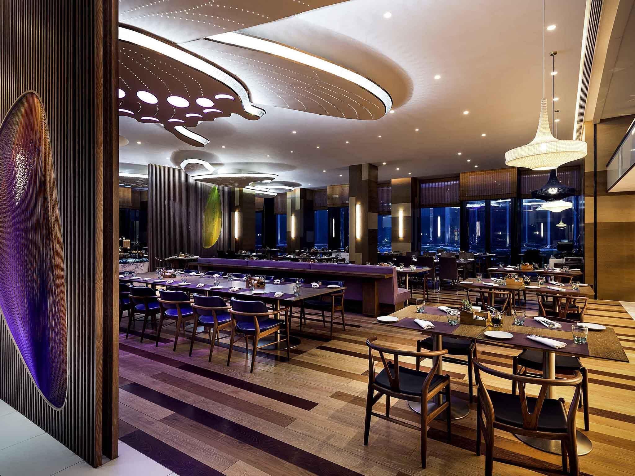 A modern restaurant with a bar area, multiple dining tables, and a view of the cityscape through large windows.