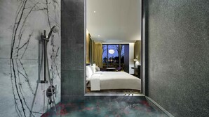 Een moderne badkamer met een marmeren vloer, een douchegedeelte, en een zichtbare slaapkamer met een bed en nachtkastje.