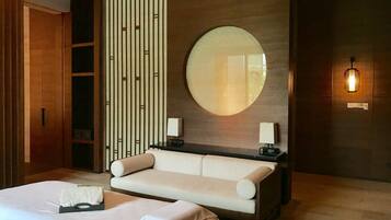 A modern hotel room with a large bed, a sofa, a round mirror, and a wall-mounted light fixture.