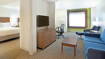 A hotel room with a bed, a TV mounted on the wall, a desk with a chair, a sofa, and a large window.