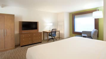 A hotel room with a large bed, a desk with a chair, a television, a wardrobe, and a window with a view.