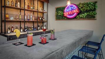Zona de bar con estantes de botellas de licor, un letrero de neón y taburetes.