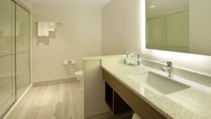 Une salle de bain moderne avec une douche à parois de verre, des toilettes blanches et un comptoir en granit doté d’un lavabo et d’un miroir.