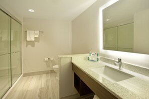 Une salle de bain moderne avec une douche à parois de verre, des toilettes blanches et un comptoir en granit doté d’un lavabo et d’un miroir.